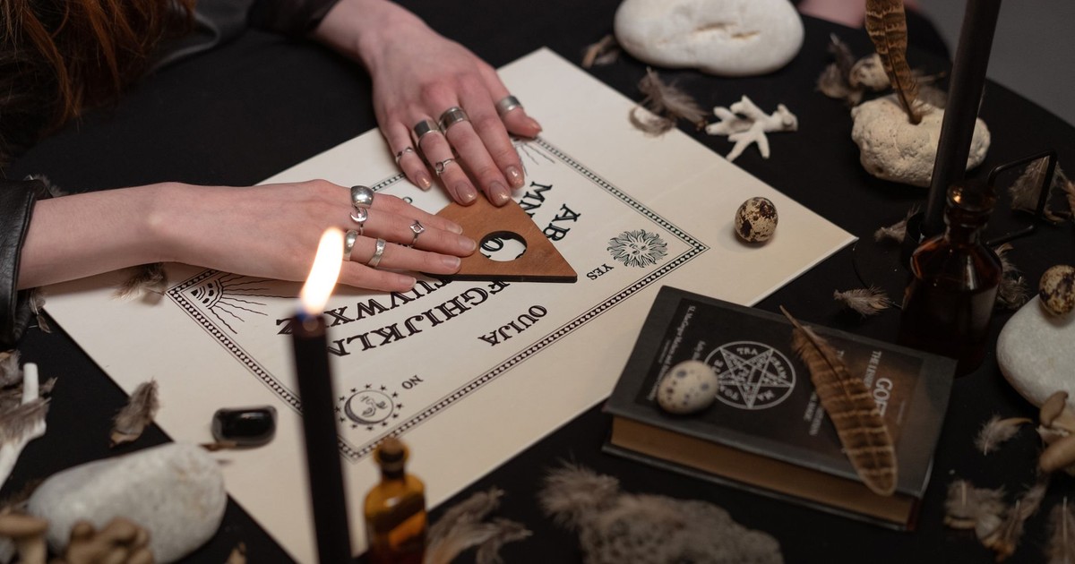 A mystical setup featuring ouija board, candles, feathers, and spiritual items creating a mood of mystery and mysticism.