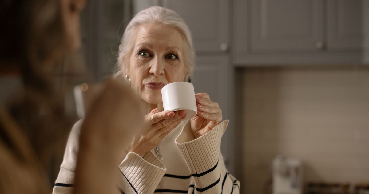 Senior woman with white hair holding a ceramic cup while drinking tea indoors