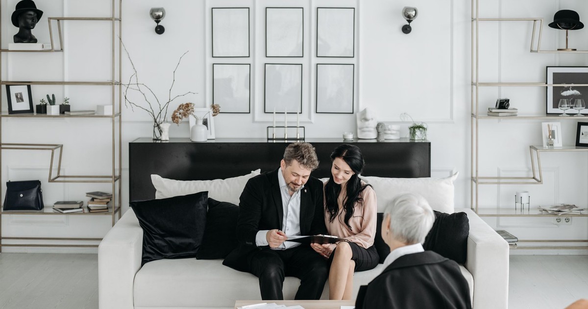 Couple consulting with a social worker in a modern living room setting, discussing documents.