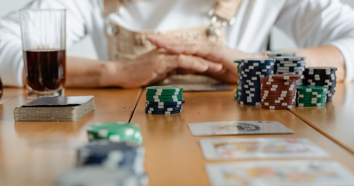 Senior woman playing poker with cards and chips on a wooden table indoors.
