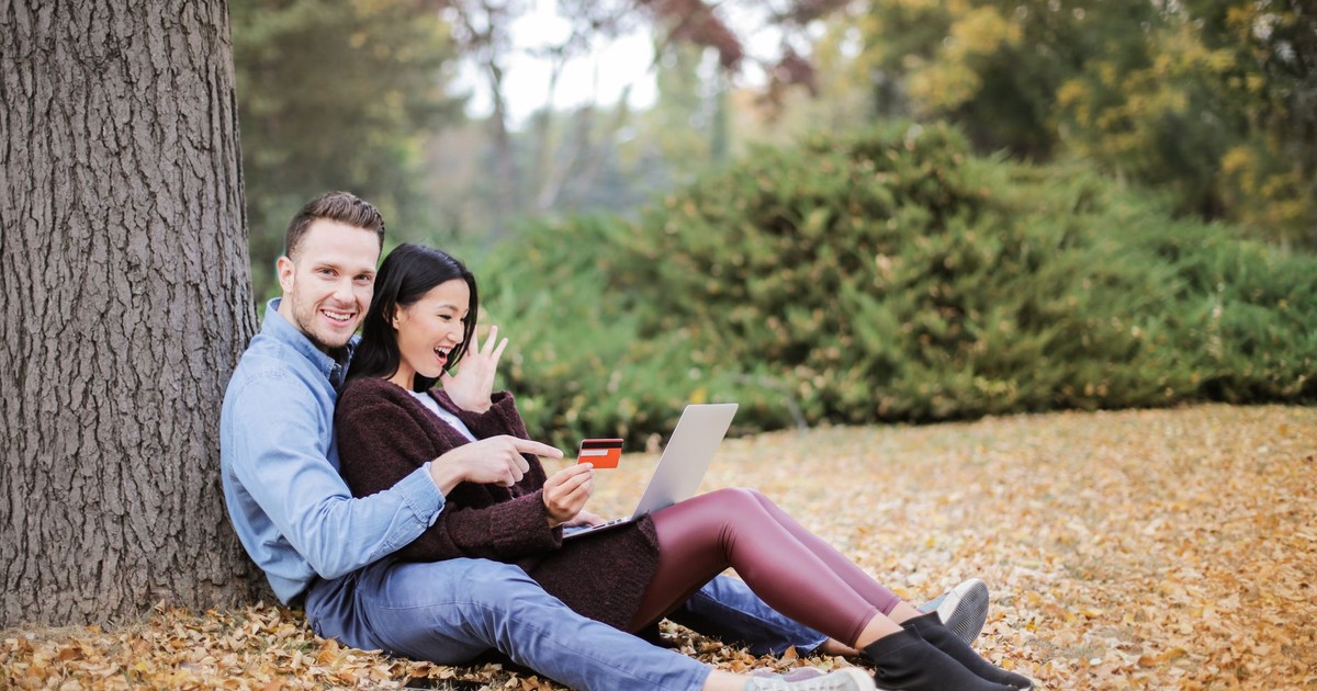 A joyful couple using a laptop and credit card outdoors during fall.