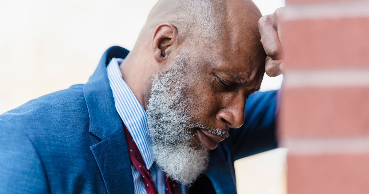 Side view of concerned bald African American male entrepreneur in classy suit leaning on brick wall while standing on street