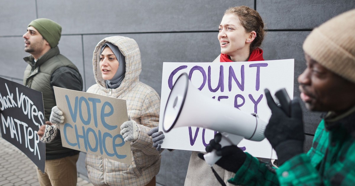A diverse group of adults holding protest signs advocating for voting rights, standing outdoors.