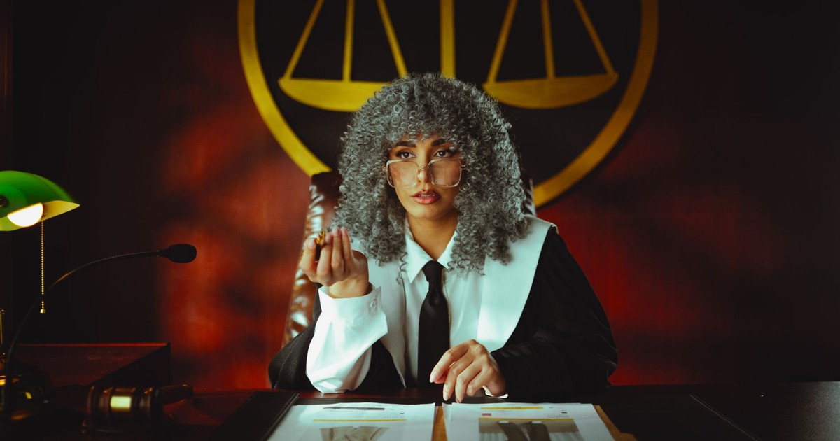 Portrait of a judge in a courtroom with the scales of justice emblem in the background.