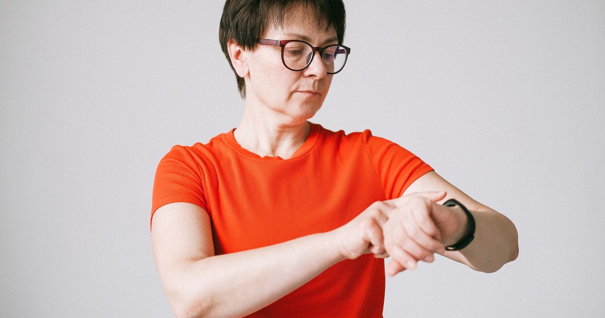 A woman in glasses checks her smartwatch in a minimalist indoor setting.