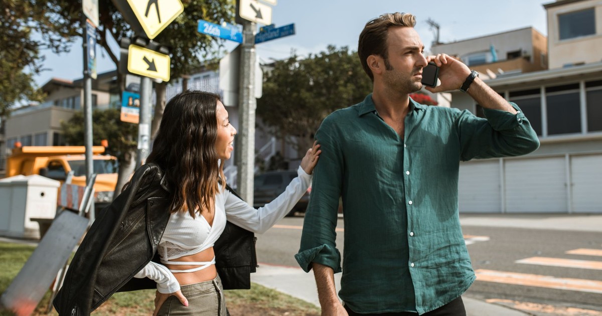 A couple has an intense discussion outdoors on a sunny street corner.