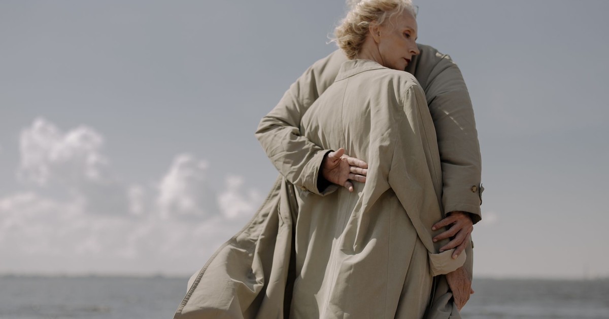 Elderly couple embracing lovingly by the ocean, conveying warmth and companionship.