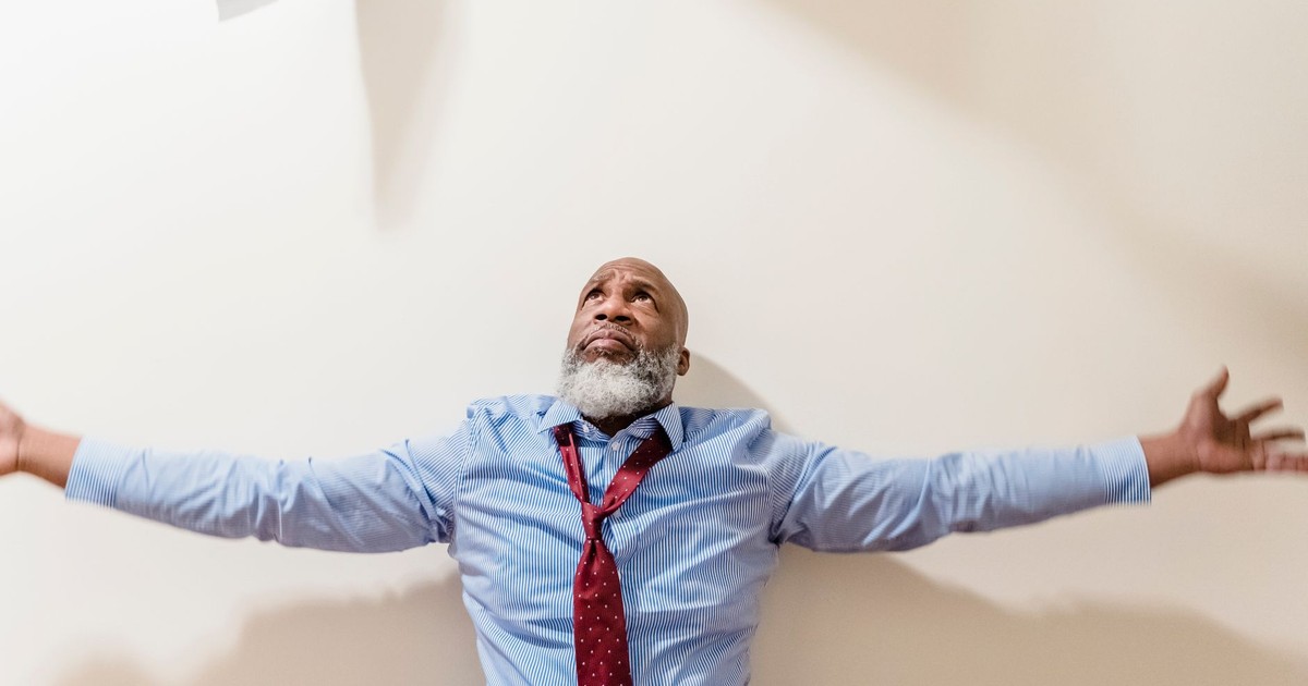 A frustrated businessman with arms outstretched, expressing vulnerability and stress indoors.