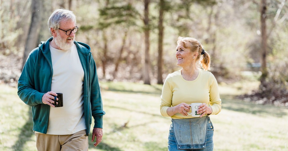 Happy elderly couple walking outdoors, sharing a joyful conversation with warm smiles.