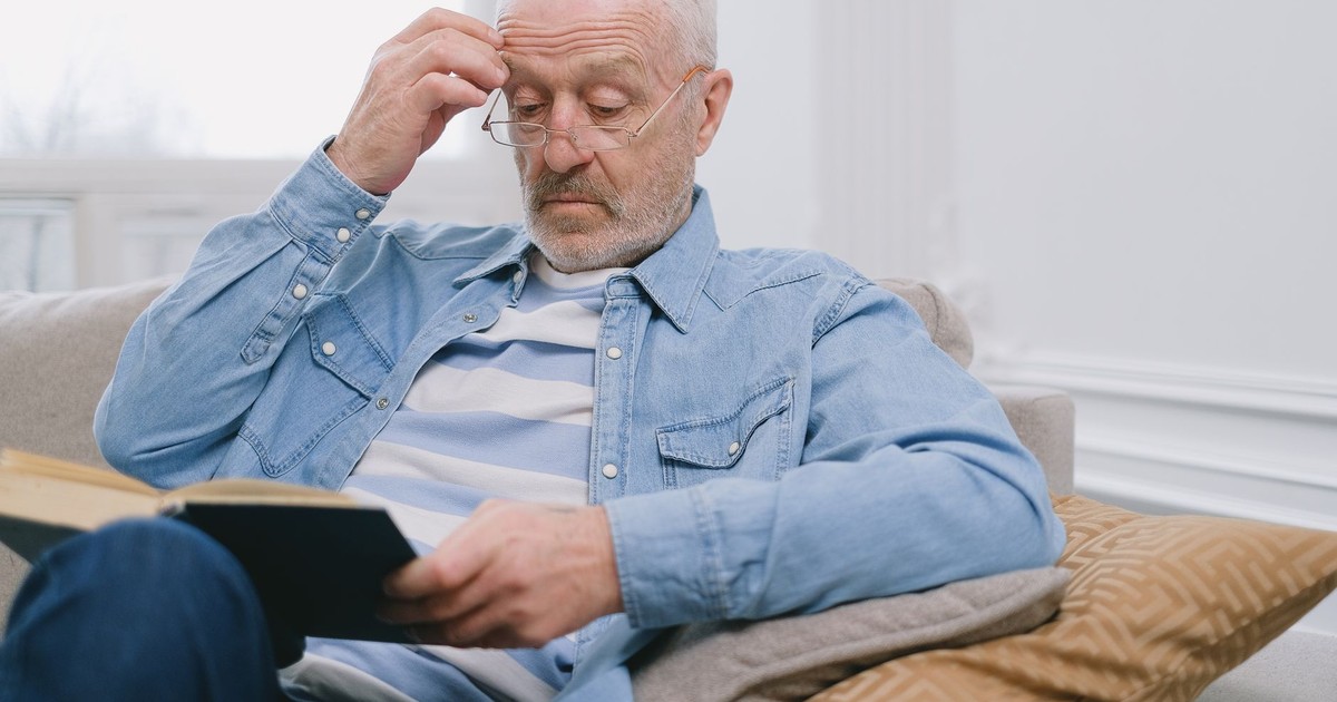 Senior man with glasses reading a book inside a stylish living room.