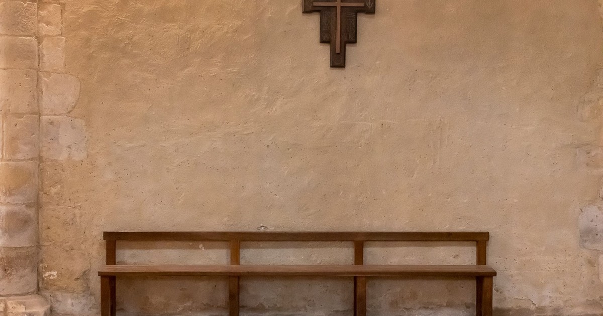 A tranquil church interior featuring a wooden pew and cross against a stone wall.