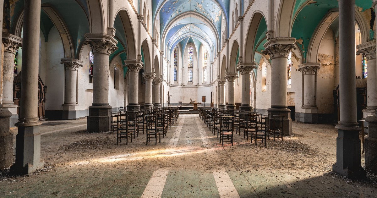 Wide-angle view of an abandoned gothic church interior featuring arched columns and scattered chairs.