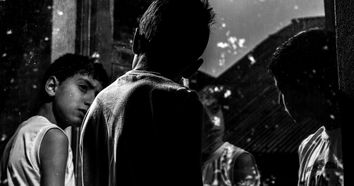 Black and white portrait of boys looking at reflections in a window.