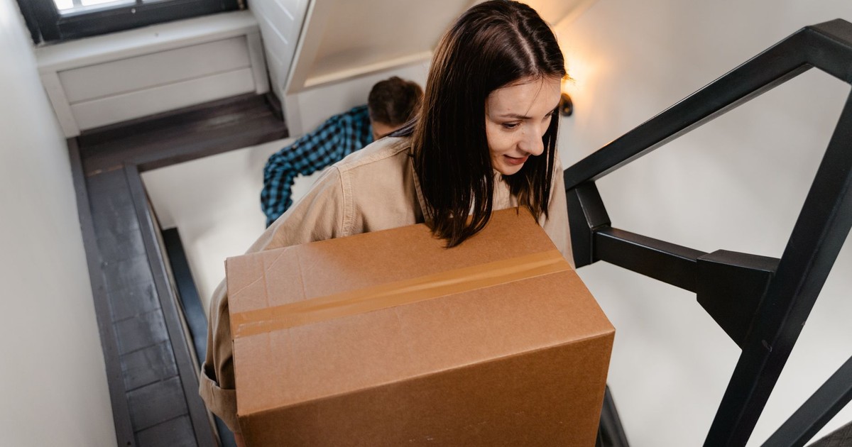 A couple carrying a large box up a staircase, symbolizing moving into a new home.