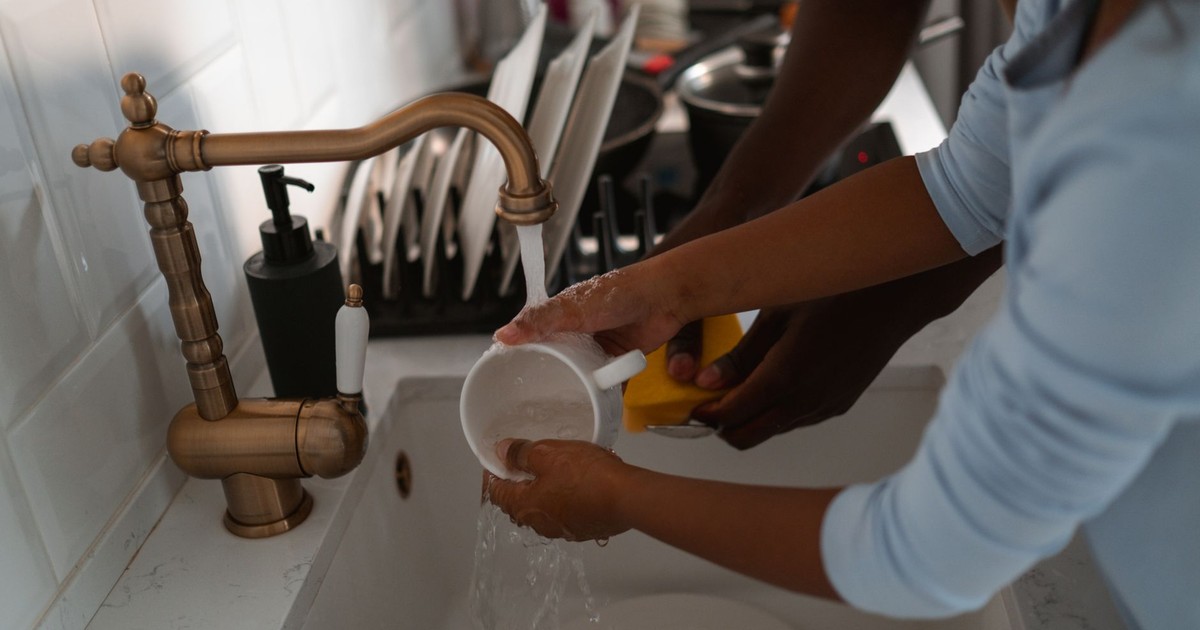 A child and adult washing dishes together at a brass kitchen sink, promoting teamwork and family chores.