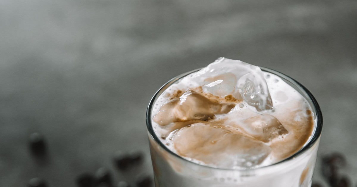 Close-up of a chilled iced coffee with frothy milk and ice cubes in a glass against a muted background.
