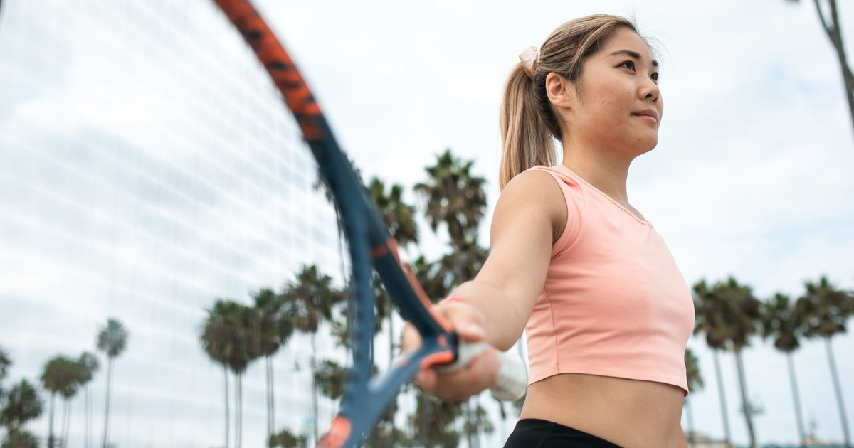 Active woman playing tennis in park with palm trees surrounding