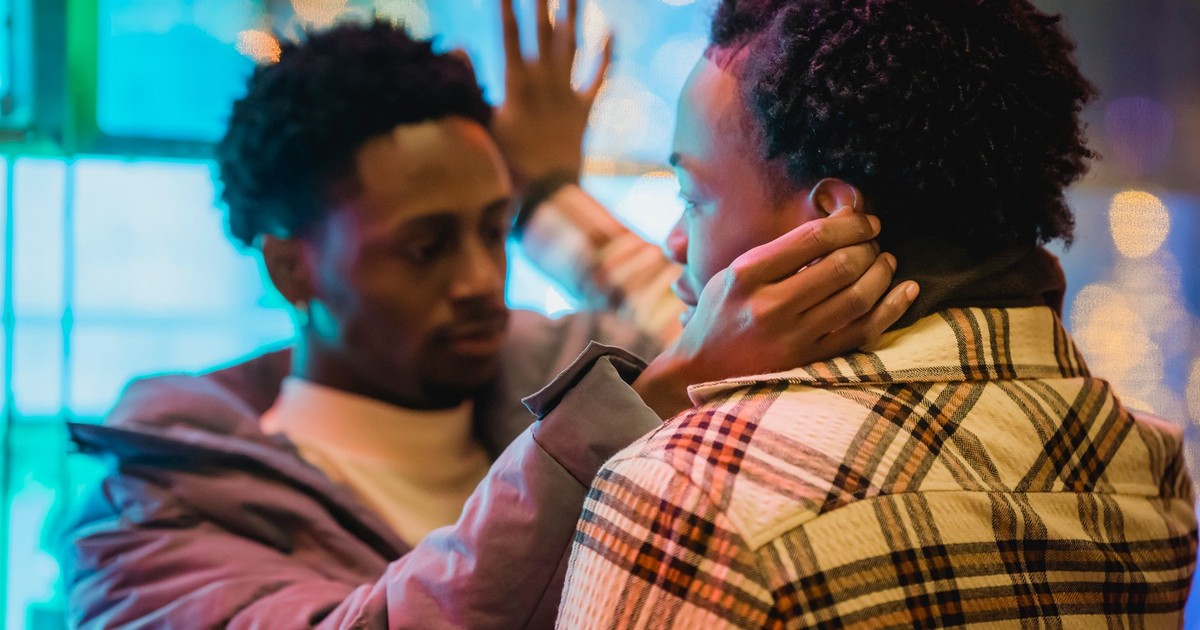 African American men touching each other while leaning on window of building in evening