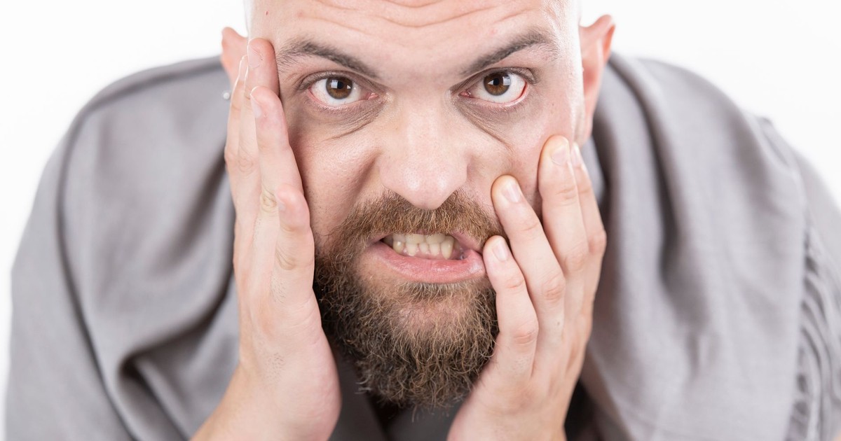 Close-up of a bearded man showing frustration with hands on face.