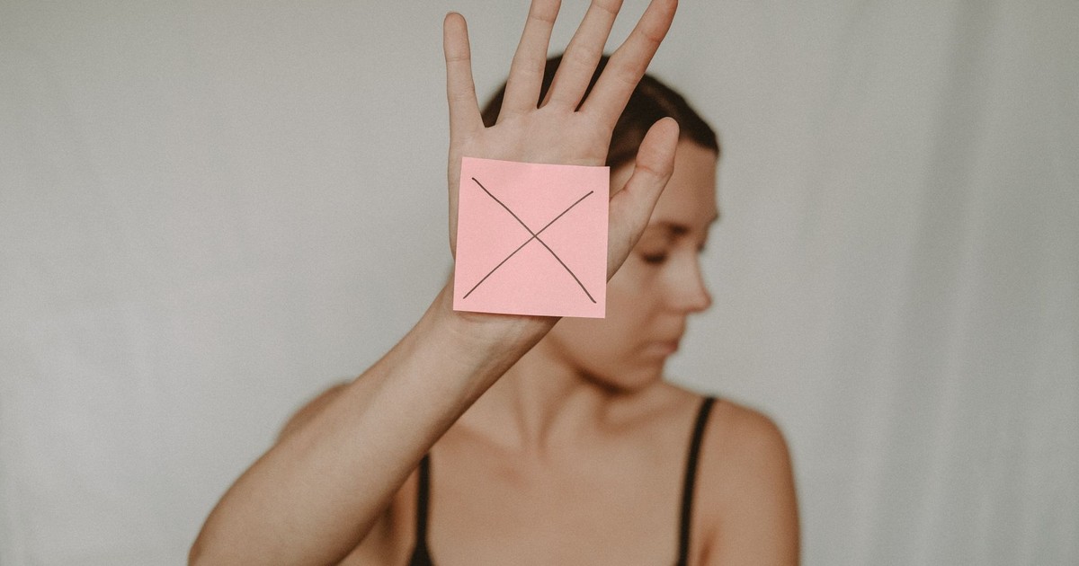 Young slender woman with closed eyes demonstrating sign stop with sticker on palm