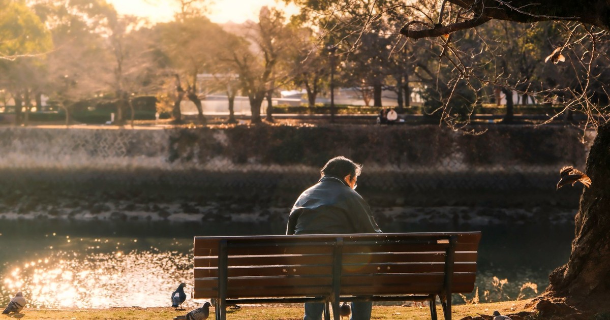 Peaceful scene of man on bench by river in Hiroshima during sunset.