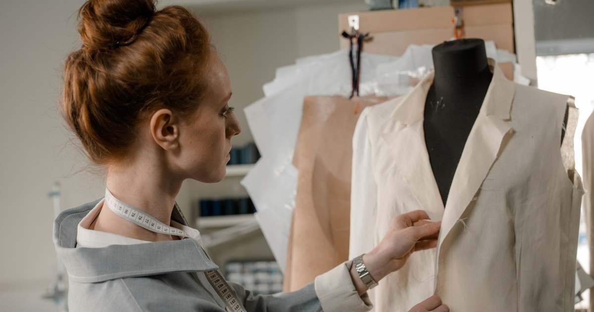 A woman tailor carefully working on a dress on a mannequin in her studio.