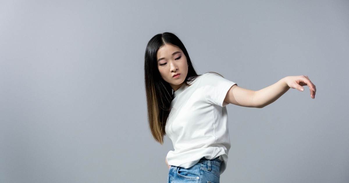 Asian woman in white shirt and denim jeans posing gracefully against a plain backdrop.