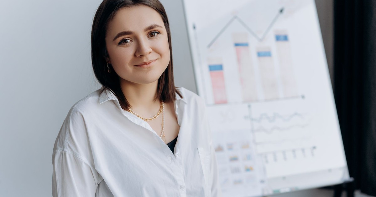 Smiling woman in a white shirt presents business graphs on a flipchart in a modern office.