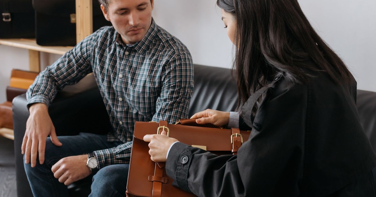 Two adults discussing a luxury leather briefcase in an office setting.
