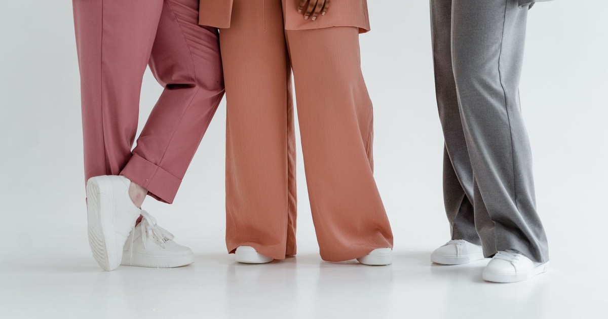 Three people wearing stylish wide-leg pants and white sneakers on a white background. Studio shot.