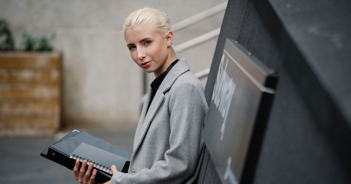 Side view attractive young businesswoman in gray coat standing with documents in folder on street