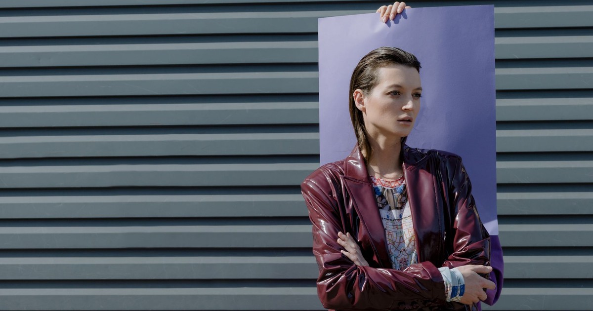 Fashionable woman in burgundy leather jacket posing against a modern background under daylight.