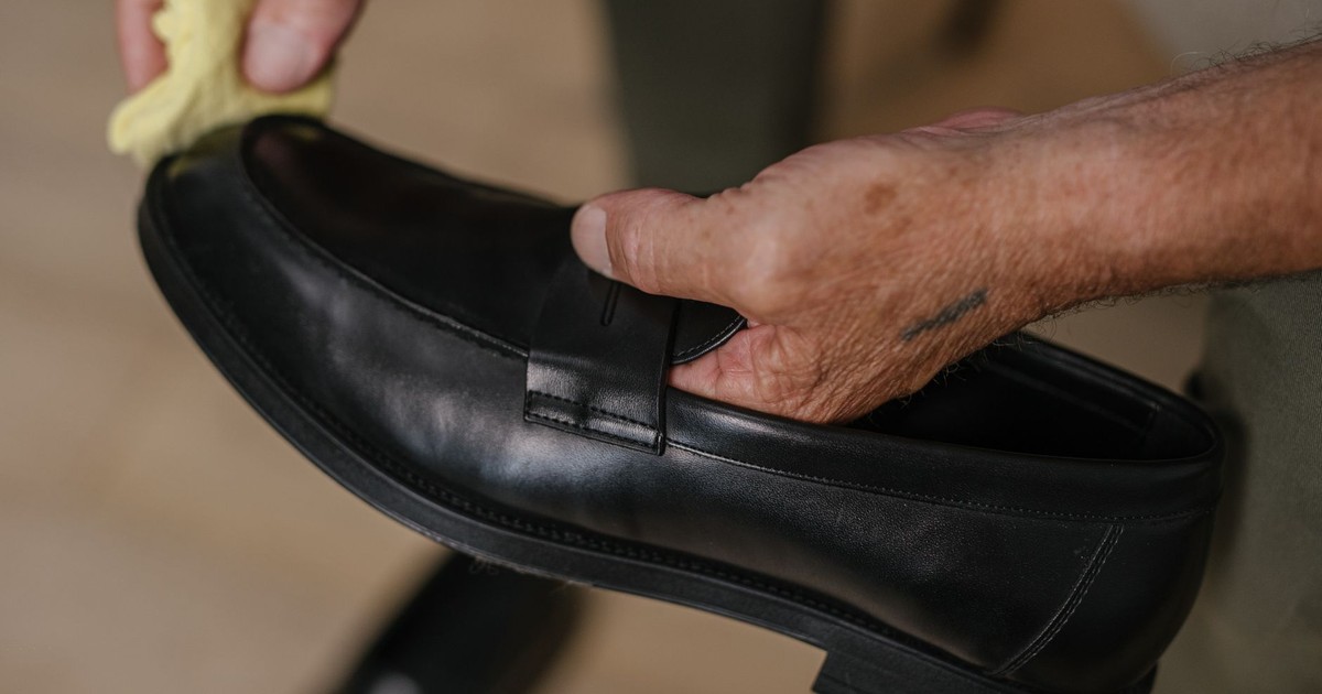 Detailed shot of hands polishing a black leather shoe with a cloth indoors.