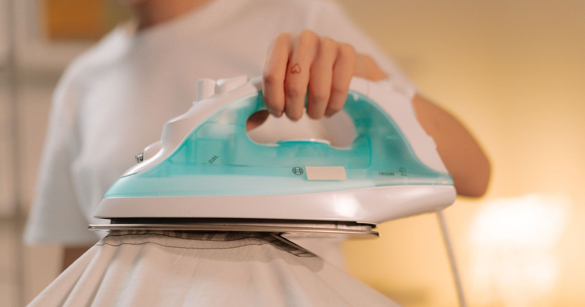 Close-up of a person using a steam iron for smoothing a white garment indoors.