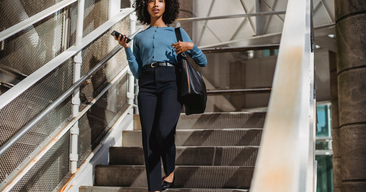African American woman walking down stairs holding smartphone and bag.
