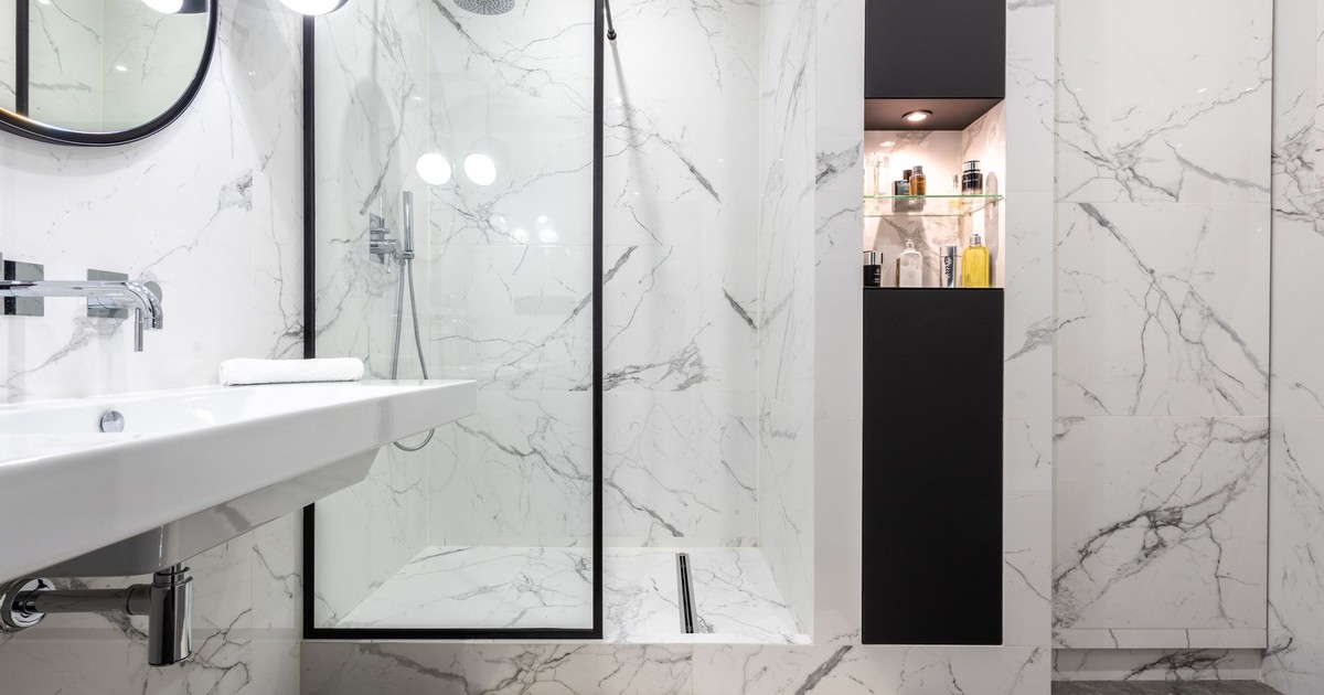 Modern bathroom interior with shower room against bottles of perfumes and washbasin under mirror reflecting shiny lamp in house