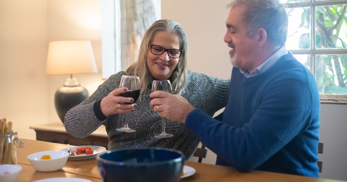 Senior couple smiling and toasting with wine indoors, celebrating a moment of togetherness.