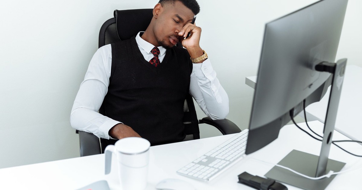 A man in business attire resting his head at an office desk, displaying workplace fatigue.