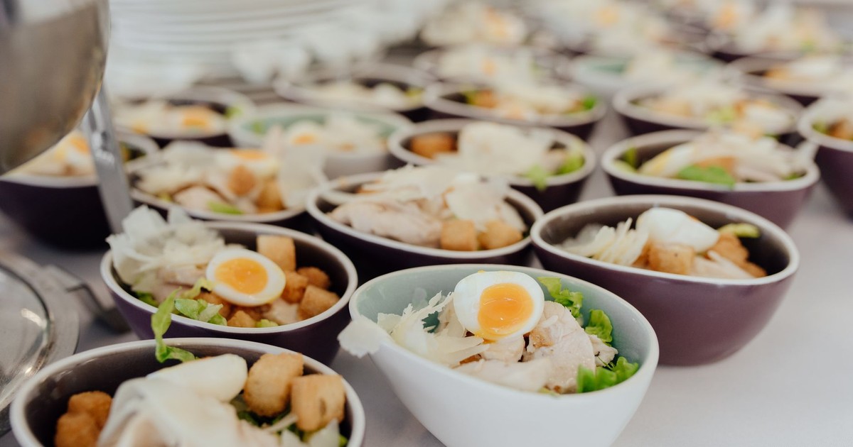 Salads with chicken crackers and boiled eggs served in bowls on table with dishware on blurred background in light cafe