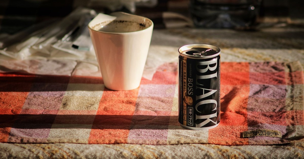 Close-up of a can of black coffee and a porcelain mug on a checkered tablecloth.