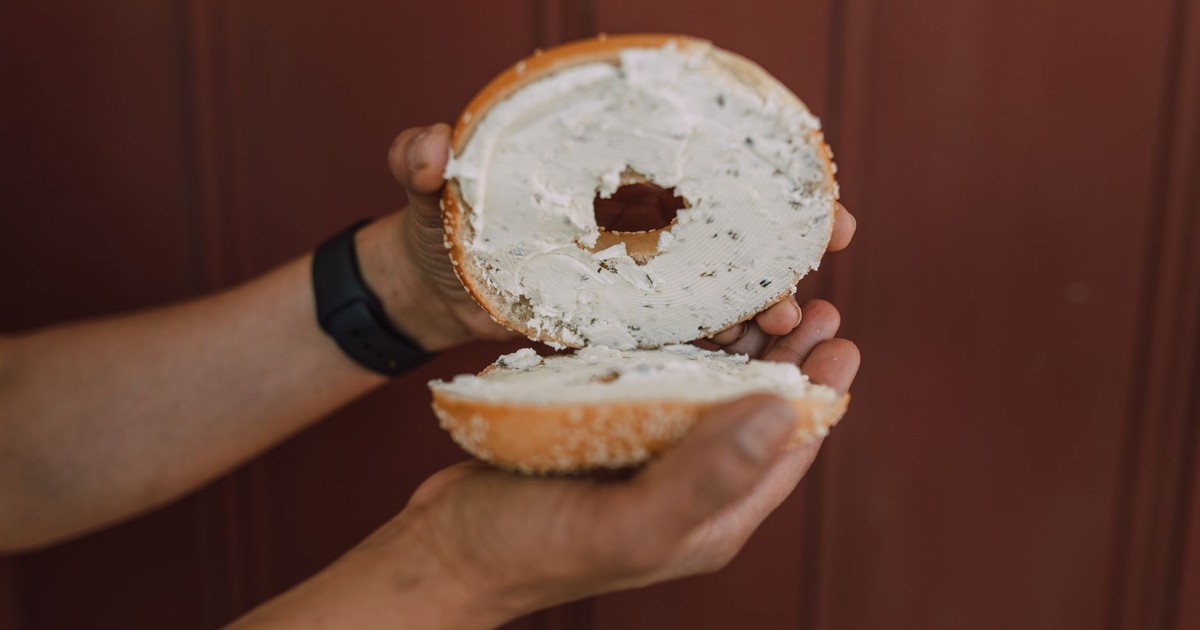 Person holding a freshly sliced bagel with cream cheese, perfect for breakfast or snack.