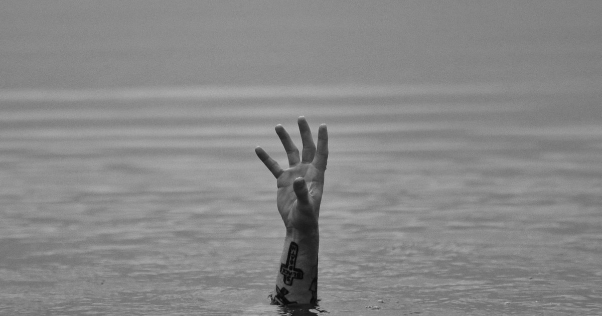 A tattooed hand reaches up from the water, creating a dramatic monochrome scene.