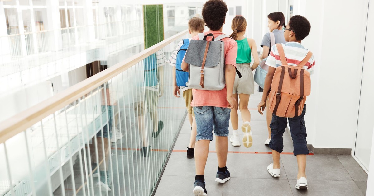 Group of children walking inside a modern school hallway with backpacks.