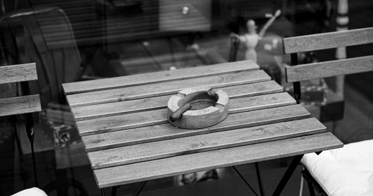 Monochrome image of a wooden patio table with an ashtray and cigar outdoors.