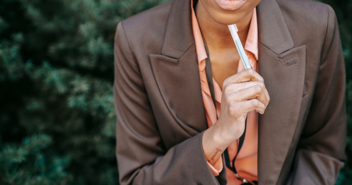 High angle of crop female entrepreneur in formal wear touching chin with pen while thinking on solution in park