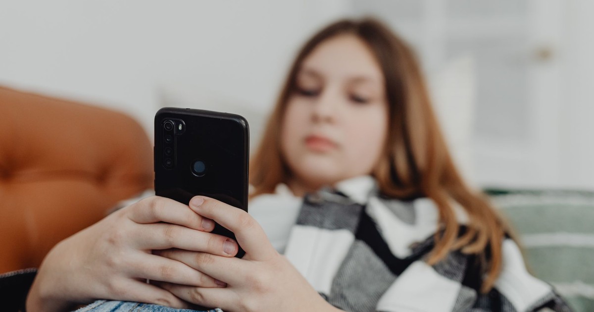 Teenage girl using smartphone while relaxing on a sofa, depicting leisure and connectivity.