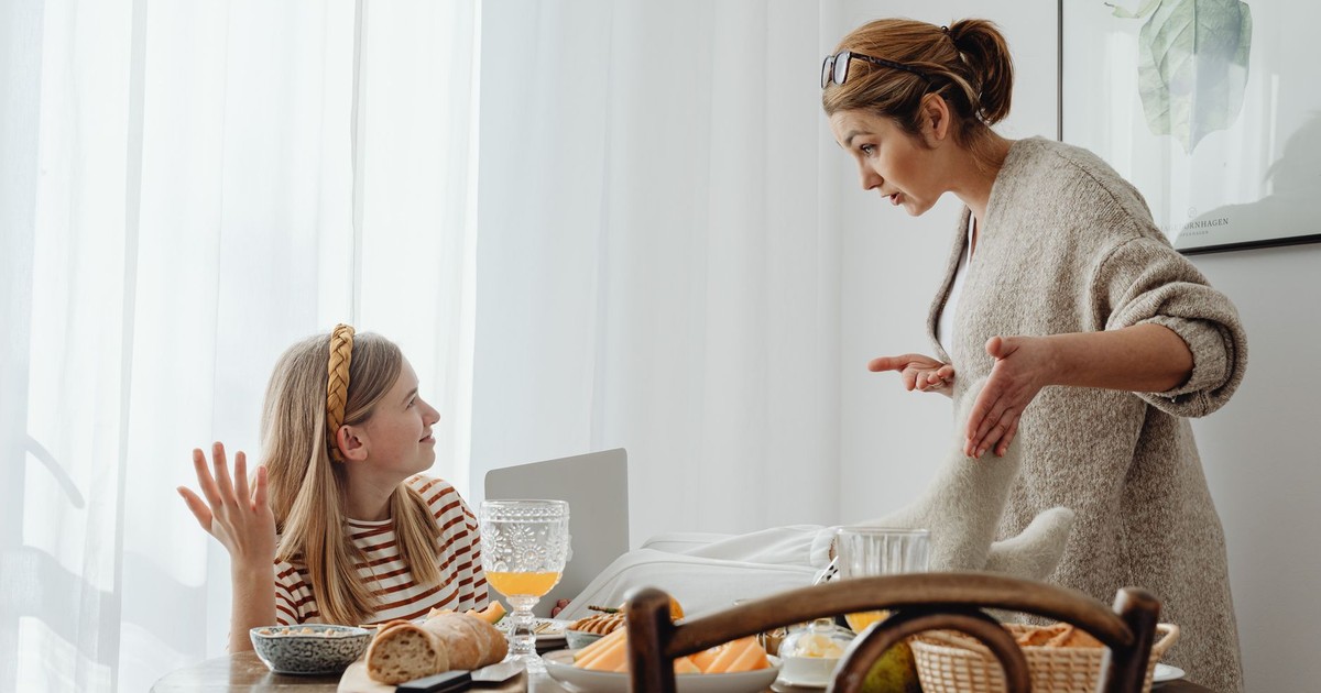 A mother and teenage daughter having a discussion while having breakfast at home.