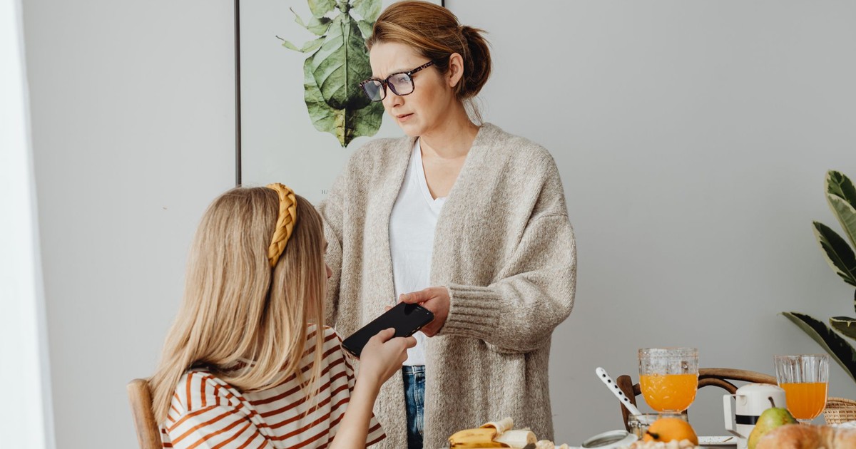 A mother correcting her teenage daughter's behavior during breakfast, conveying parenting dynamics.