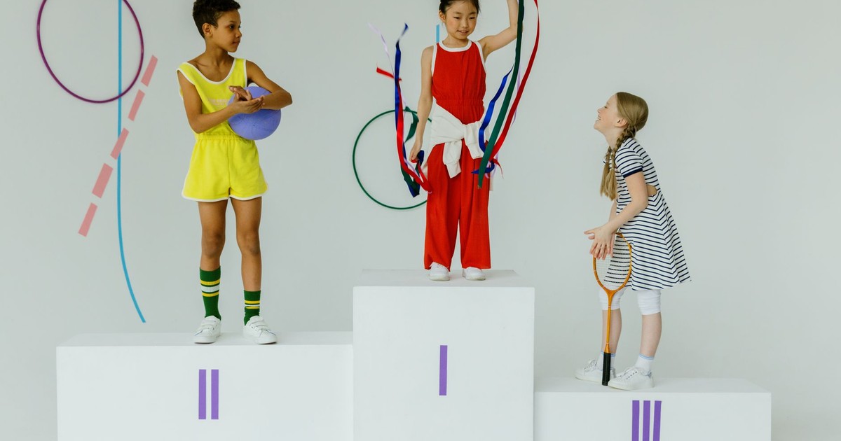 Three happy children celebrating on a gymnastics podium with equipment.