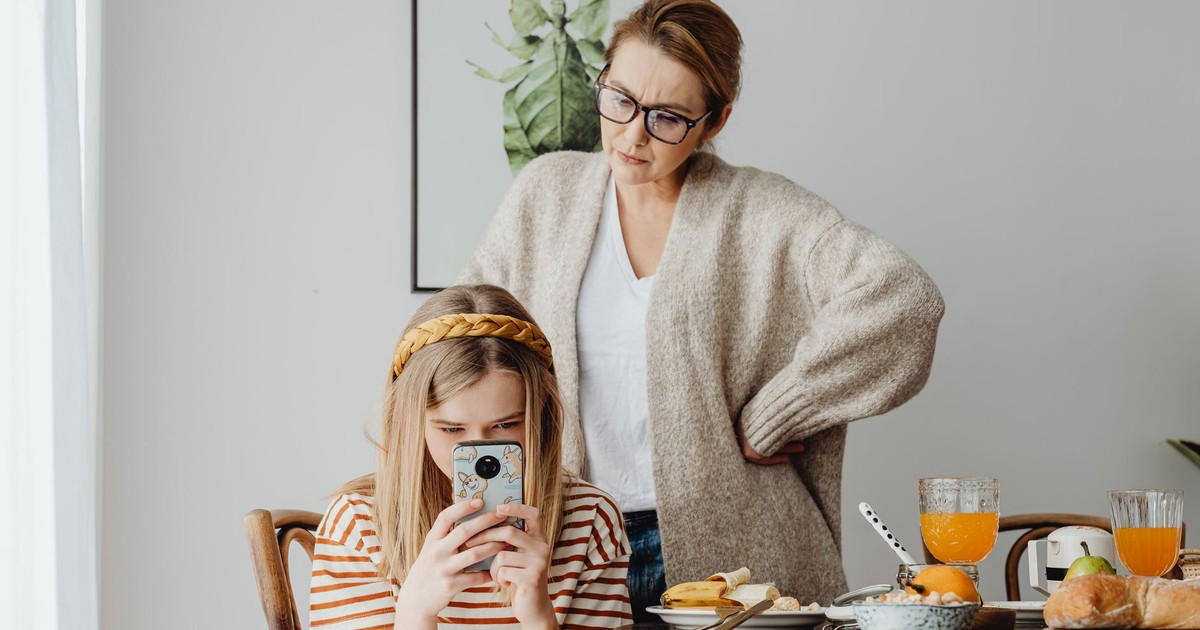 A mother looking at her daughter absorbed in a phone during breakfast. Modern family dynamics.